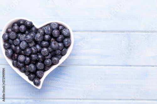 Fresh blueberries, in a heart shaped bowl on a wooden background.