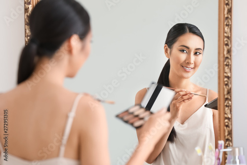 Asian woman applying makeup at home