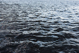 Dark water surface background with small waves and reflections. Dangerous deep river.