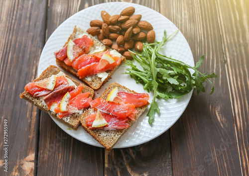 Wholemeal bread with salmon on white plate. Arugula and almond with lemon. Healthy sandwiches. Omega-3 for snack. Proper nutrition. Sport food.