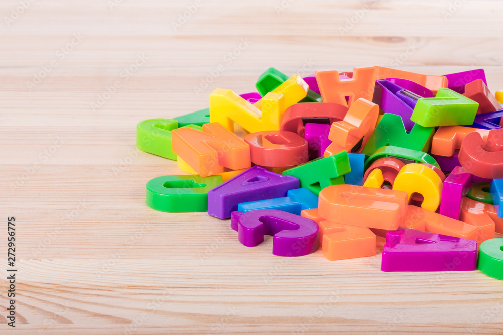 Naklejka premium A pile of coloured magnetic letters over a school wooden table