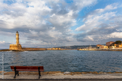 Lonely wooden bench on the waterfront of the Greek city of Chania against the background of the lighthouse