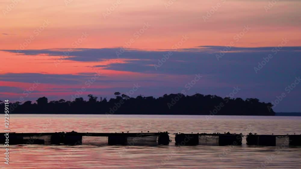 Fishing cages under cloudy orange evening sky at Lake Victoria. Birds sit on the cages. Forested island by the horizon. Kalangala, Uganda. Fishing cages under cloudy orange evening sky at Lake Victoria. Birds sit on the cages. Forested island by the horizon. Kalangala, Uganda.