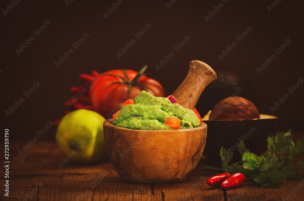 Fresh guacamole in wooden bowl with ingredients on rustic table. Fresh guacamole in wooden bowl with ingredients on rustic table.