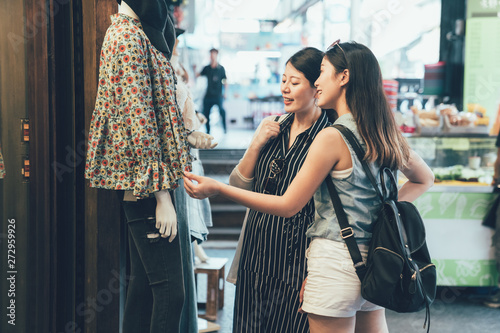 Two female shopaholic friends gazing at lady clothes wear on dummy model. sisters spend leisure time on weekend buying dress prepare for coming summer. women touching discussing about shirt hong kong photo