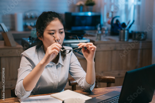 tired asian japanese woman employee businesswoman sitting at wood kichent at home in night take off glasses staring at laptop screen relax. young female worker put on eyeglasses continue work