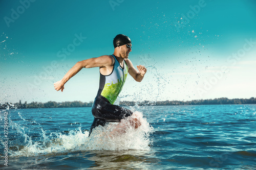 Professional triathlete swimming in river's open water. Man wearing swim equipment practicing triathlon on the beach in summer's day. Concept of healthy lifestyle, sport, action, motion and movement. photo
