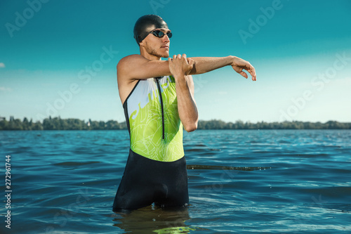 Professional triathlete swimming in river's open water. Man wearing swim equipment practicing triathlon on the beach in summer's day. Concept of healthy lifestyle, sport, action, motion and movement.