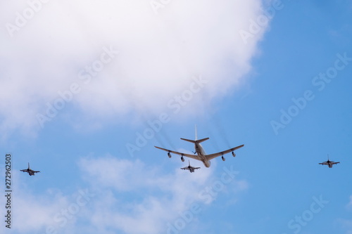 Military tanker aircraft (refueler) and fighter jets fly on blue sky and clouds background