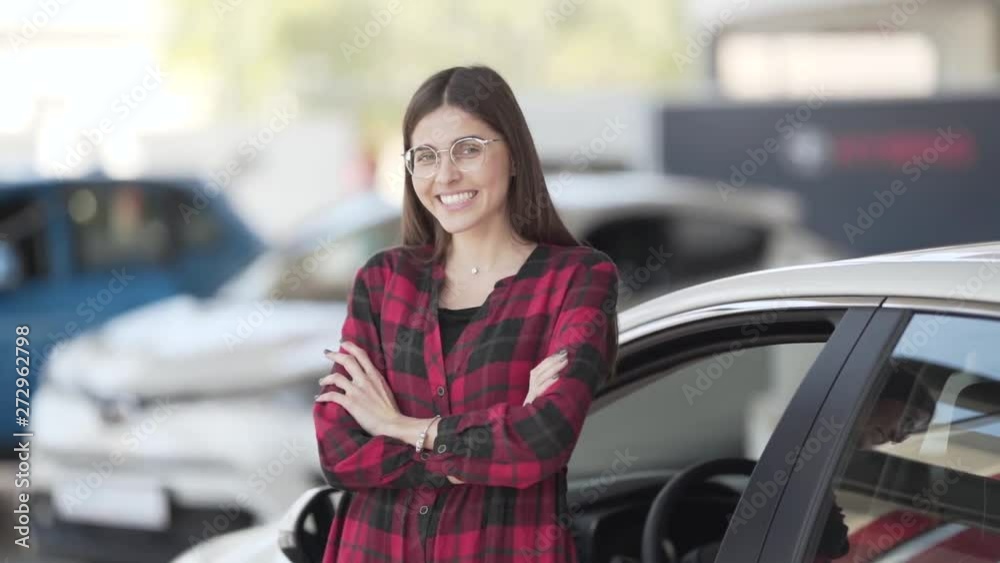 A cheerful, young woman stands inside a car dealership and smiles at the camera. A cheerful, young woman stands inside a car dealership and smiles at the camera.