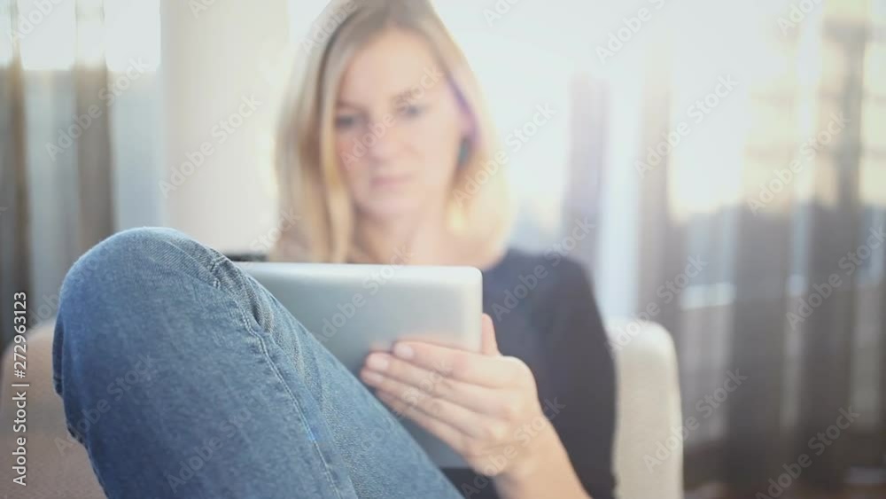 A woman, sitting on the couch, reading something on a web-connected tablet. Handheld close-up shot, with focus on her leg. A woman, sitting on the couch, reading something on a web-connected tablet. Handheld close-up shot, with focus on her leg.