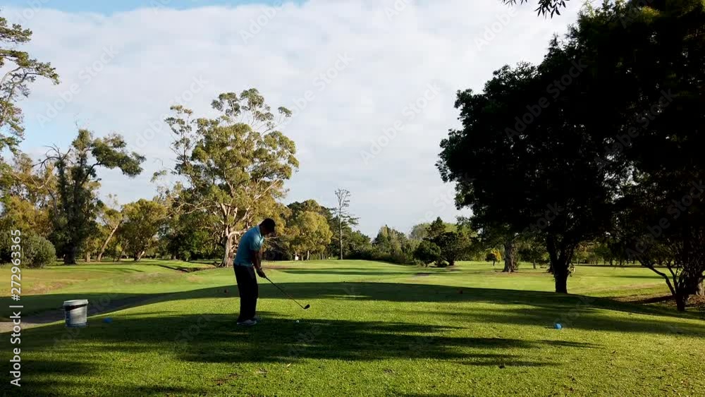 Golf course man on the tee with iron swing and hit the ball towards the green wide shot Golf course man on the tee with iron swing and hit the ball towards the green wide shot
