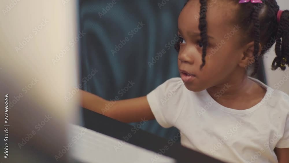Portrait of curious excited little african girl looking at monitor working on computer at desk. Cute sociable kid. Children and technology concept. Portrait of curious excited little african girl looking at monitor working on computer at desk. Cute sociable kid. Children and technology concept.