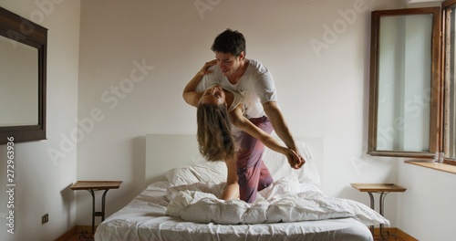 Fotografija Portrait of young just married couple wearing pajamas having fun to dance in the bedroom in the early morning in a sunny day