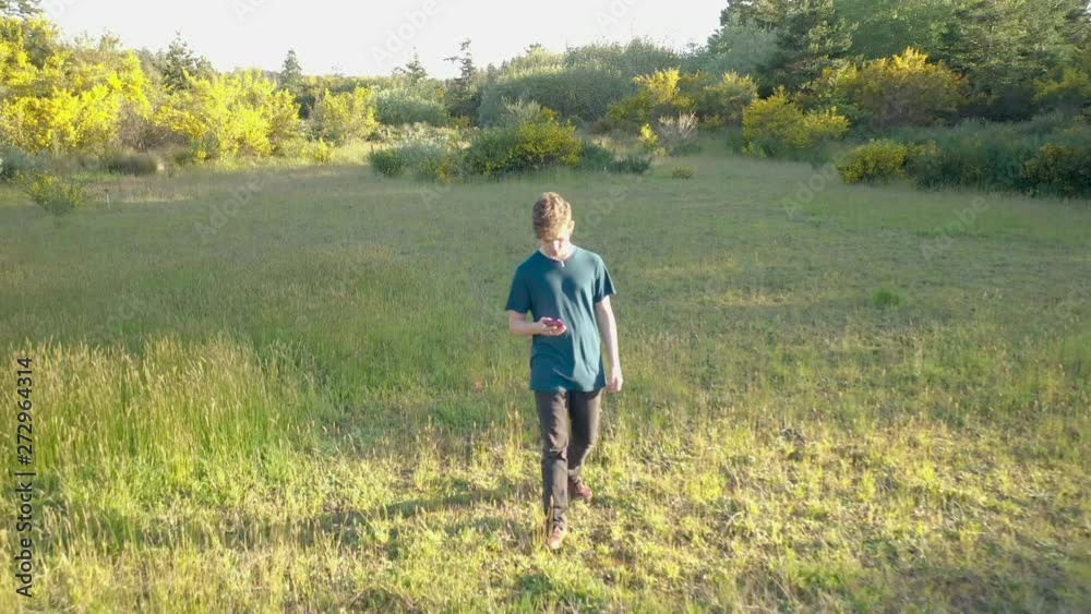 Teenage boy showing signs of gadget addiction. Walking through beautiful nature and looking at his phone. Teenage boy showing signs of gadget addiction. Walking through beautiful nature and looking at his phone.