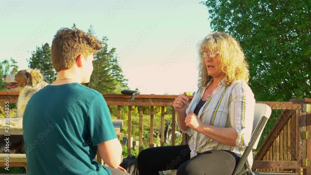 A woman teaching a teenage boy sign language. Relaxed outdoor setting with dogs present.