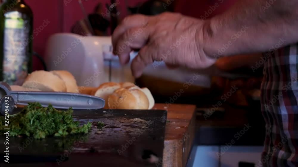 Handheld Shot of Elderly Womans Hands Cutting Bread With a Knife In an Old Kitchen With Basil, Olive Oil and a White Toaster in The Background Handheld Shot of Elderly Womans Hands Cutting Bread With a Knife In an Old Kitchen With Basil, Olive Oil and a White Toaster in The Background