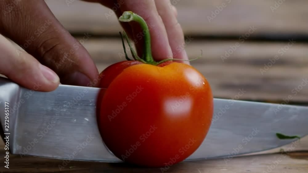 Close up with slowmo of hands of unrecognizable man cutting juicy tomato in half Close up with slowmo of hands of unrecognizable man cutting juicy tomato in half