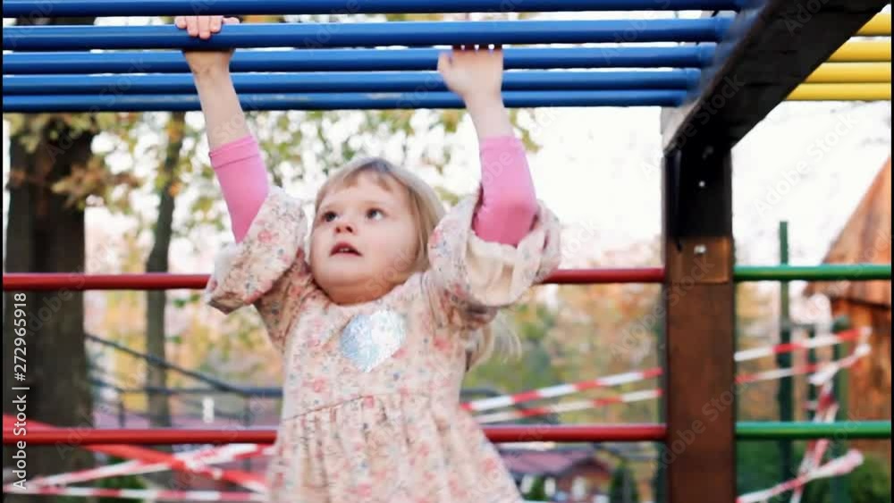 A cute little girl exercise on monkey bars; she climbs successfully and jumps when she reaches the end; handheld HD video, rack focus