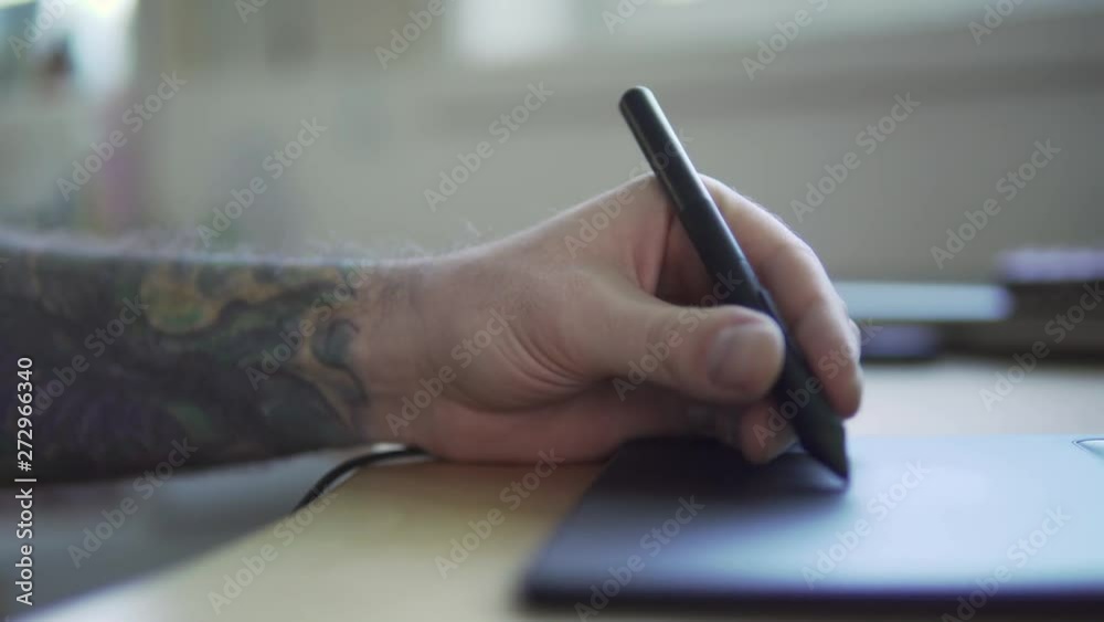 A person with a tattooed arm is drawing something on a graphic tablet. A person with a tattooed arm is drawing something on a graphic tablet.