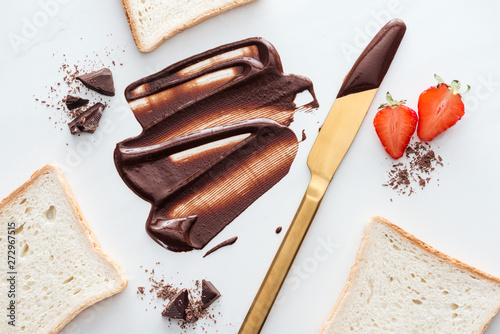 Top view of gold table knife with liquid chocolate, pieces of chocolate bar, strawberries and toasts