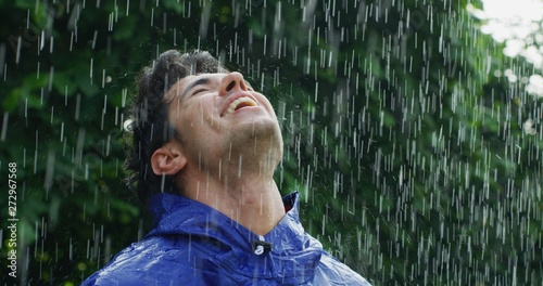 Foto Portrait of young carefree handsome young man wearing protection cape is feeling free under the rain on a background of green trees