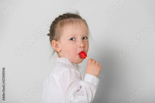 Cute little girl in white shirt sucks red Lollipop. On white background.