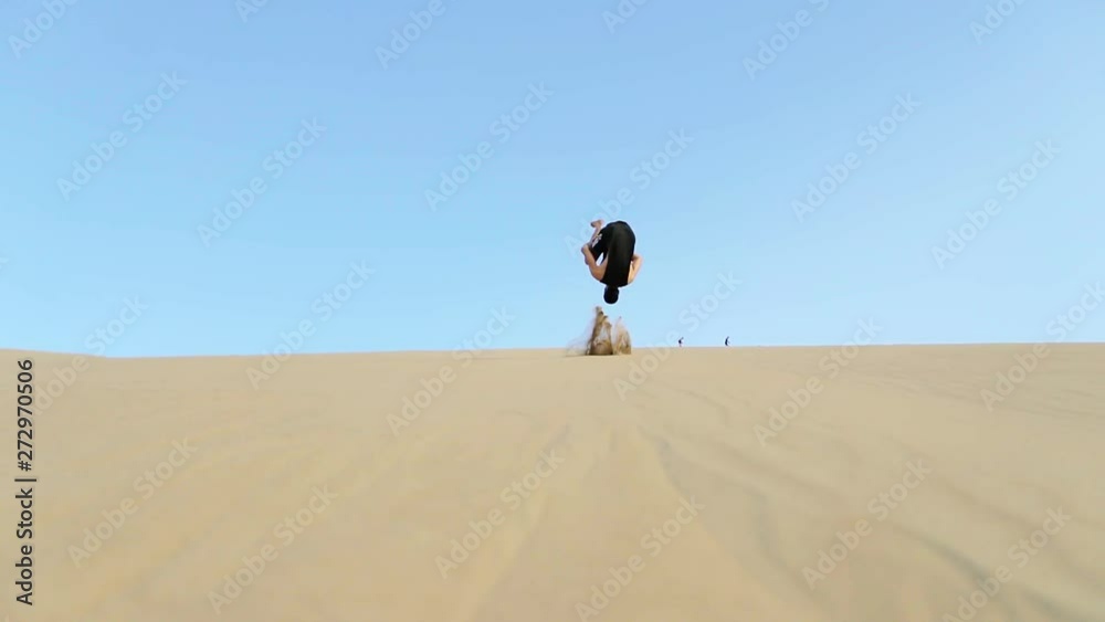A young man performs an impressive front flip on the sand dunes of Huacachina, Peru A young man performs an impressive front flip on the sand dunes of Huacachina, Peru