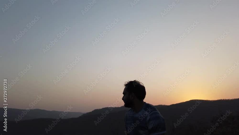 Young Man Sitting on a Rock During Sunset Across a Valley with Beautiful Scenery Young Man Sitting on a Rock During Sunset Across a Valley with Beautiful Scenery