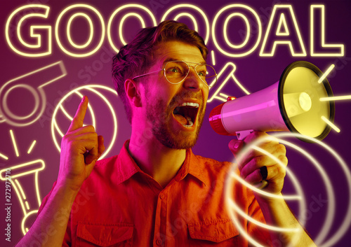 Young man as a sport's fan on purple background in neon light. Male model screaming, cheering for the favourite football or soccer team. Concept of facial expression, summer, vacation, sport, betting.