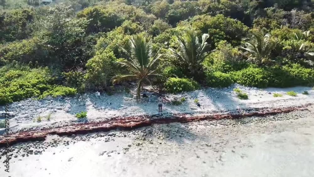 Traveling bearded Millennial man flying drone selfie on tropical island vacation zooming out on Caribbean rocky sandy beach with ocean waves crashing in the bay Traveling bearded Millennial man flying drone selfie on tropical island vacation zooming out on Caribbean rocky sandy beach with ocean waves crashing in the bay