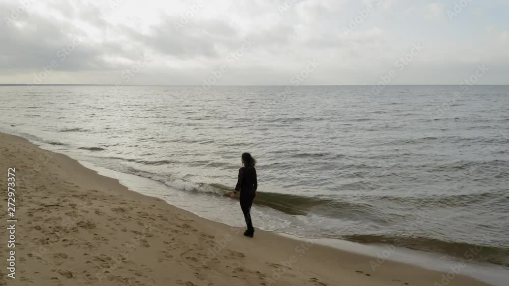 Aerial shot following a girl walking alone on the seashore Aerial shot following a girl walking alone on the seashore