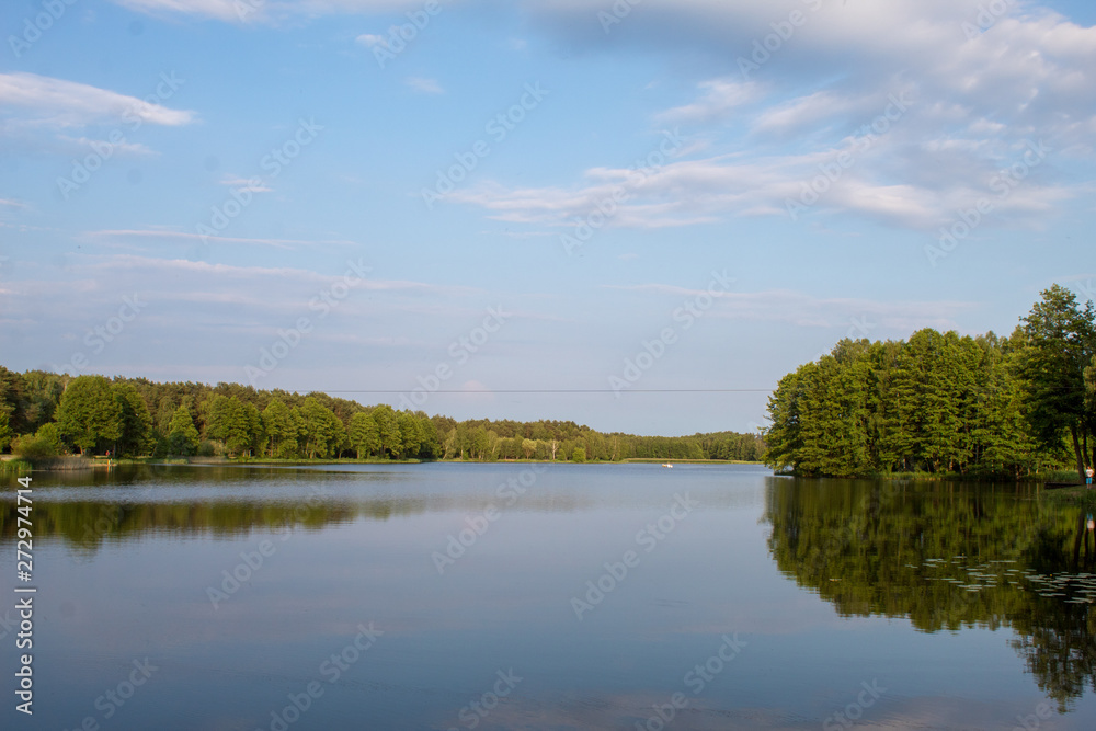 Fototapeta premium Landscape of a beautiful superficial blue lake surrounded by forest in the central part of Poland on a sunny summer day.