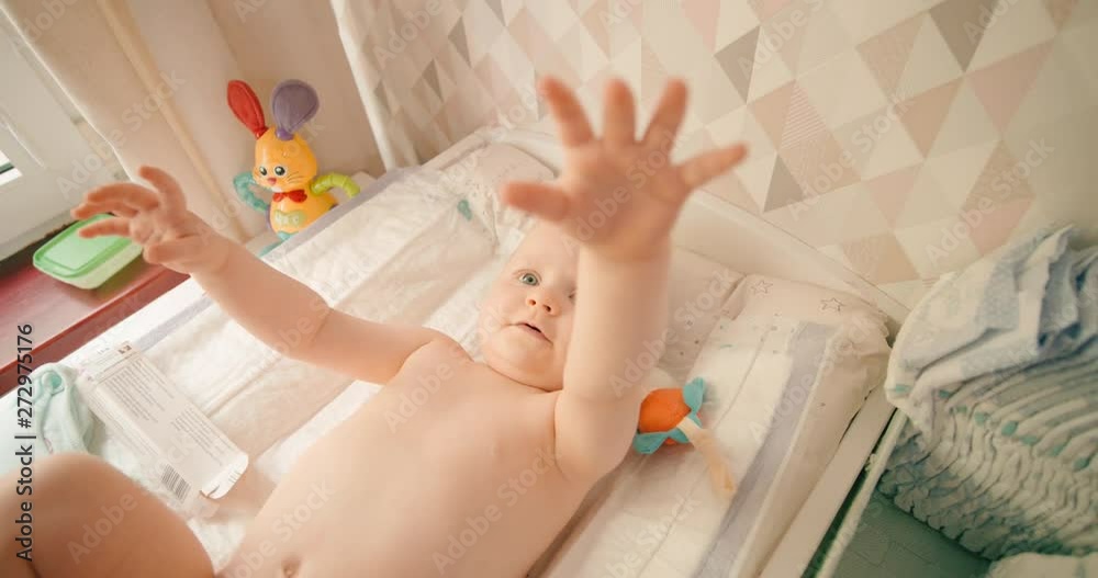 Baby girl stretches out hands on the changing mat, wants to get up