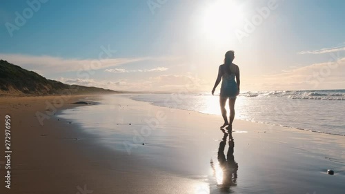 Slow motion shot of a young woman bear foot relaxed walk along the sand beach at Pardoe Northdown Conservation Area Tasmania with open ocean sand dunes and sky on the background photo