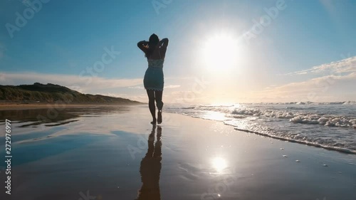 Camera following slow motion shot of a young woman bear foot relaxed walk along the sand beach at Pardoe Northdown Conservation Area Tasmania with open ocean sand dunes and sunset on the background photo