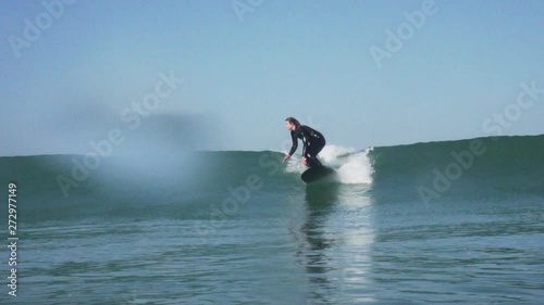 In water shot of a surfer girl riding a longboard in cold water nose riding to the end of her board on a small wave photo