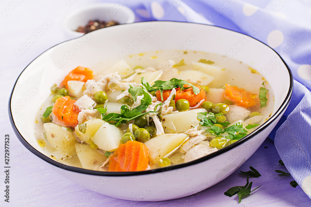 Chicken soup with green peas, carrots and potatoes in a white bowl on a light background.