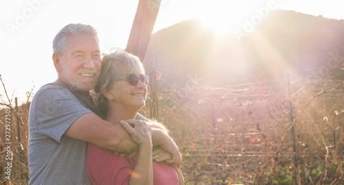 Cheerful and happy healthy people couple of senior old caucasian man and woman in outdoor leisure activity together hugging and smiling enjoying the sunset with love and forever relationghip concept