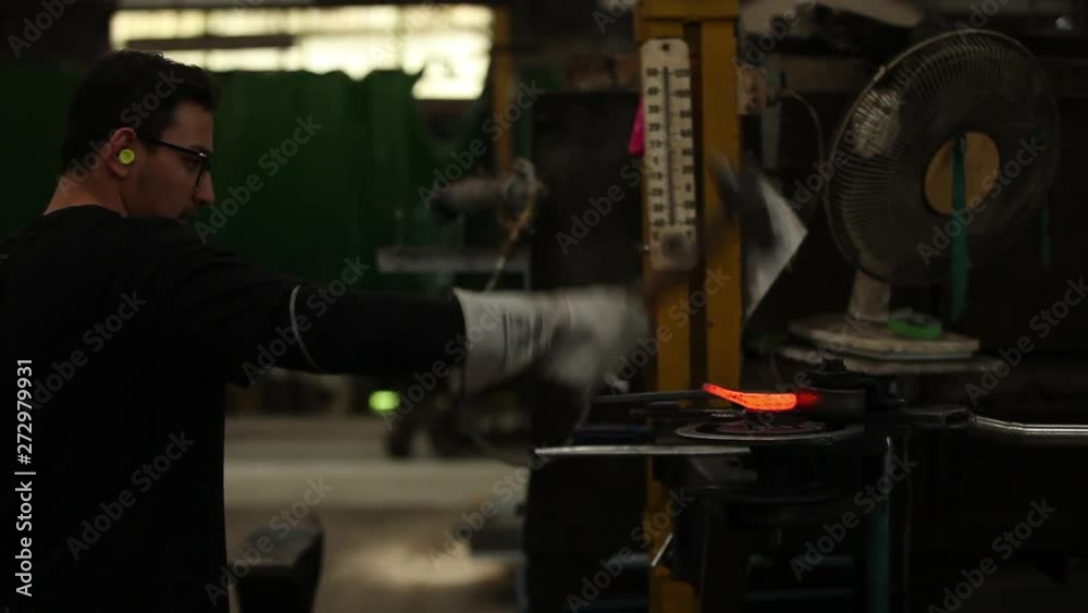 Young guy uses hammer to break metal shards away and then shifts the shape of the burning hot metal bar. Young guy uses hammer to break metal shards away and then shifts the shape of the burning hot metal bar.
