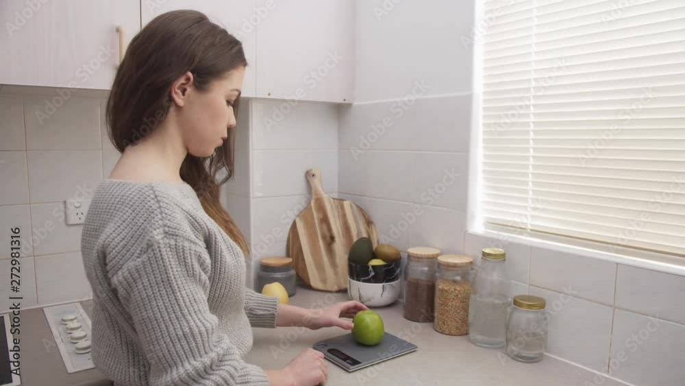 Young female using kitchen scale to weigh fruits Young female using kitchen scale to weigh fruits