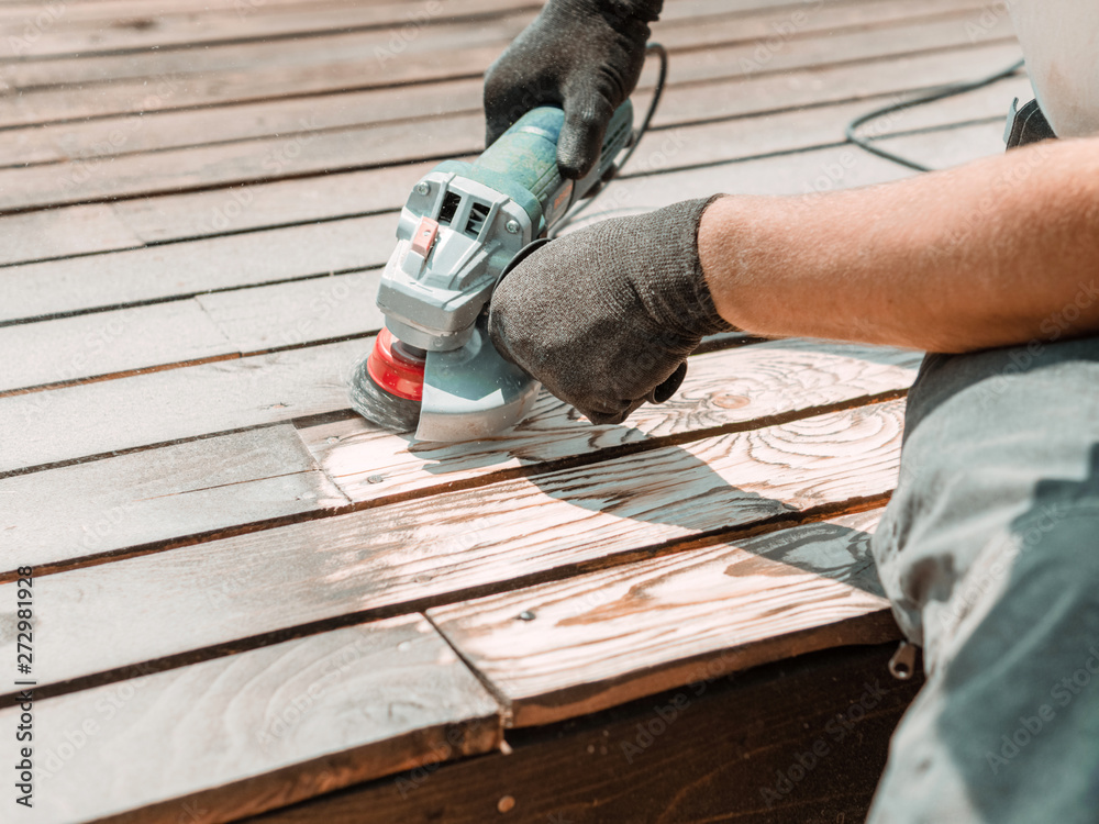 Male hands polishing dark wooden plank with angle grinder and metal brush