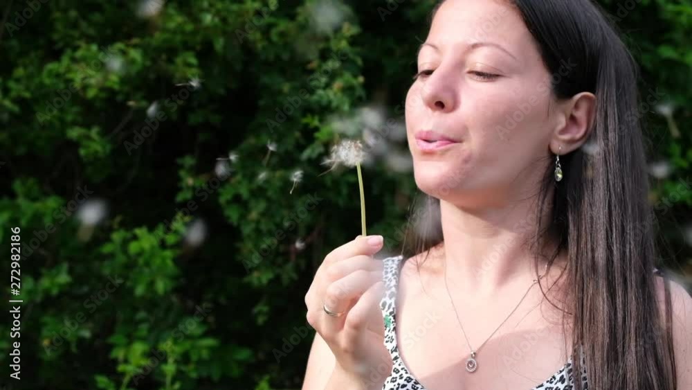 Woman blows dandelion puff ball and the seeds start flying slowly in the air. Slow Motion close up shot. Woman blows dandelion puff ball and the seeds start flying slowly in the air. Slow Motion close up shot.