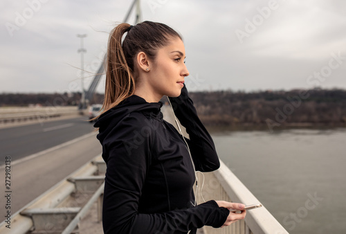 Portrait of young woman in black sports outfit resting after running on the bridge in the city. © Zoran Zeremski
