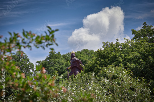 A monument to an old warrior in a helmet looks out from the trees against the sky