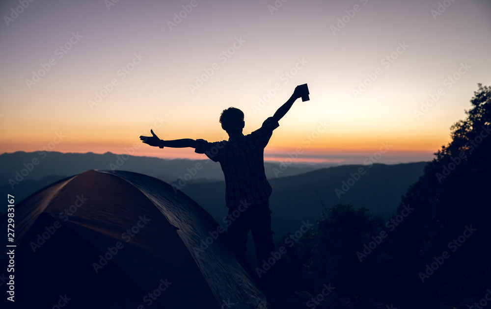 Happy hiker man holding coffee cup near camping tent on mountains at sunset background. travel concept.