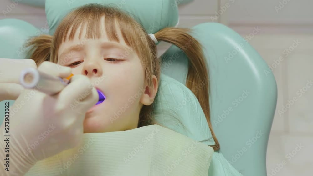 Portrait of dentist treating teeth of cute little girl sitting in dental chair, filling cavities and doing professional cleaning. Portrait of dentist treating teeth of cute little girl sitting in dental chair, filling cavities and doing professional cleaning.