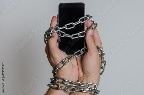 Mobile phone smartphone chained to hands with chains on a light background