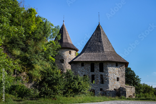 Two half-destroyed stone towers near the rock in the greenery - part of the medieval fortifications of the city of Kamianets-Podilskyi. Ukraine.