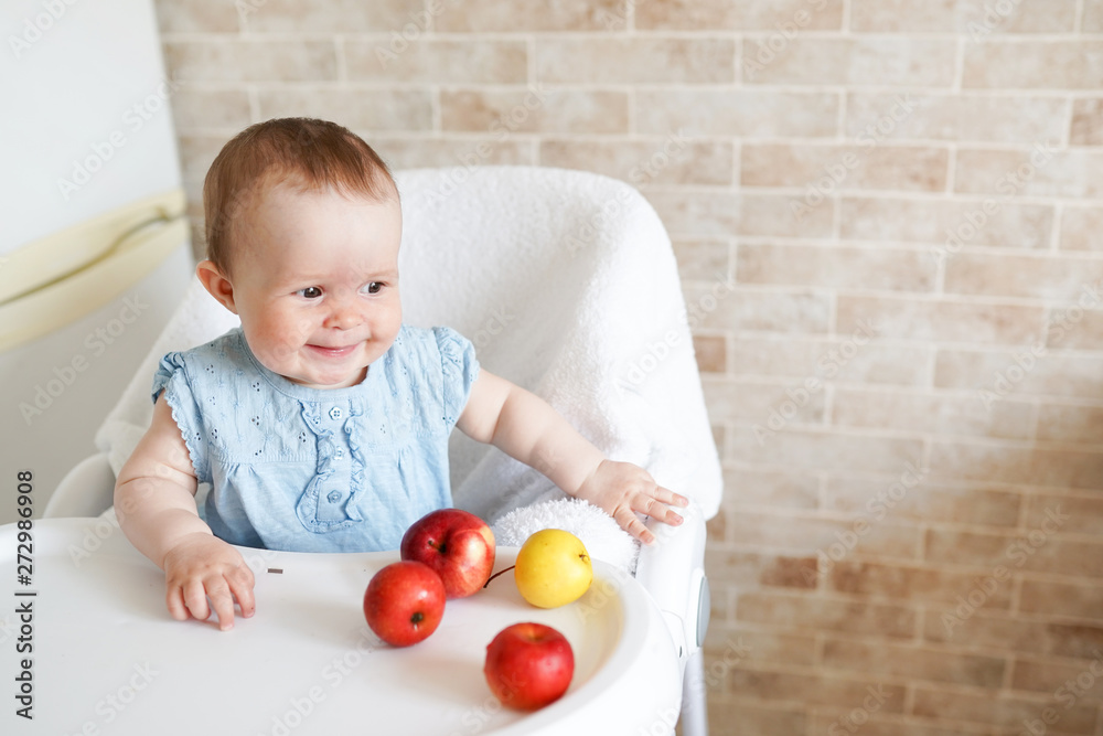Portrait of cute adorable smiling laughing Caucasian child kid girl sitting in high chair eating apple fruit Portrait of cute adorable smiling laughing Caucasian child kid girl sitting in high chair eating apple fruit